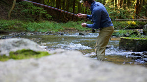 Angler mid-drift on a small wooded stream in the Approach Hoodie in Blue Run and Approach Pants in Freestone