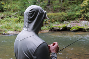 Back view of the ETHIC Approach Hoodie in Hemlock, hood pulled over a cap, rigging line beside a stream