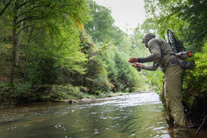 Angler wading a wooded stream to cast, wearing ETHIC Approach Pants in Freestone